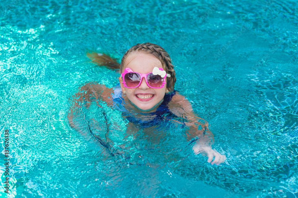 cheerful girl child resting in pool wearing sunglasses