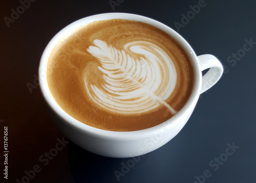 A mug of latte art coffee on black background.