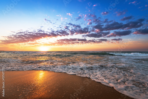 Colorful ocean beach sunrise with deep blue sky and sun rays.