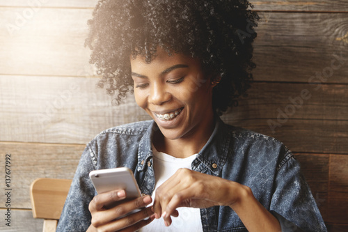 Konstfotografi Indoor shot of dark-skinned girl with cute smile and braces enjoying free wi-fi