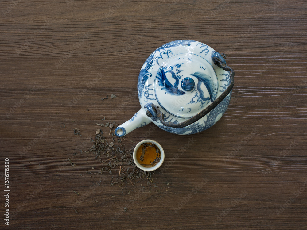 Chinese teapot and tea cup with dried tea leaf on dark brown wooden table