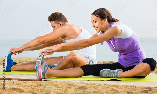 Young couple training yoga poses sitting on beach