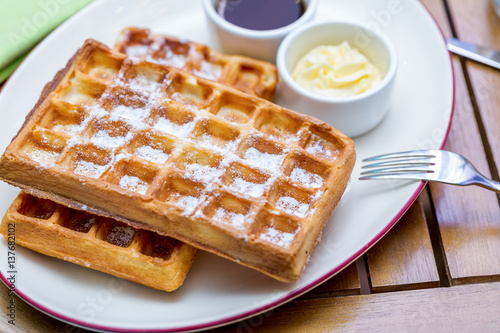 Whole wheat Belgium waffles on plate with butter, maple sauce on wooden table