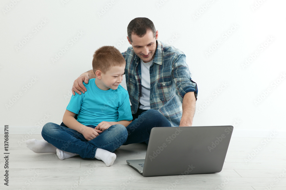Father and son using laptop sitting on the hardwood floor togeth
