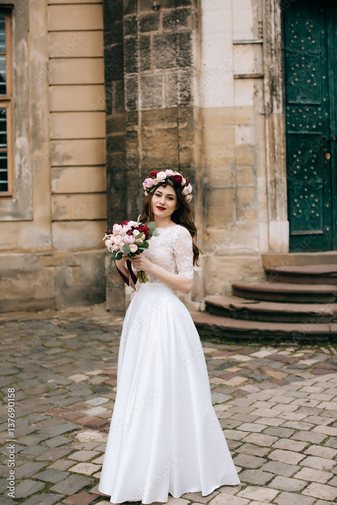 Φωτογραφία Beautiful bride with a bouquet of flowers and a wreath on the background of an o