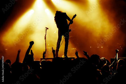 silhouette of guitar player in action on stage in front of concert crowd