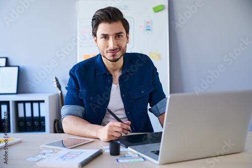 Portrait of freelance graphic designer sitting at desk with laptop and tablet photo