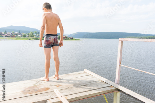 Young boy relaxes on a tower for jumping into water. Boy resting near the lake. Swimmer in shorts. summer rest. teenager sunbathe. jumping into the water from a great height. fear of high altitude
