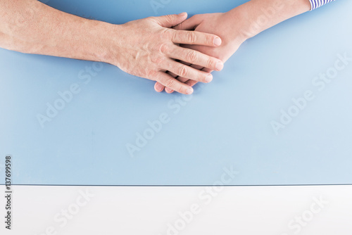 Man's hand is on top of a woman's hand. Blue background.