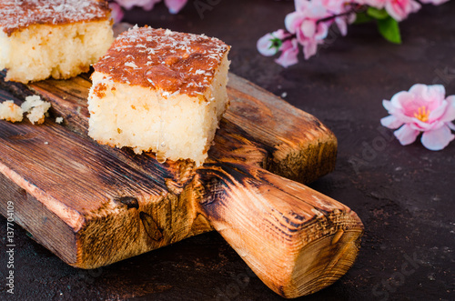 Sweet pie Basbousa or revane or Namoora on wooden plate and dark background with spring flowers. Arabian cuisine. Selective focus photo