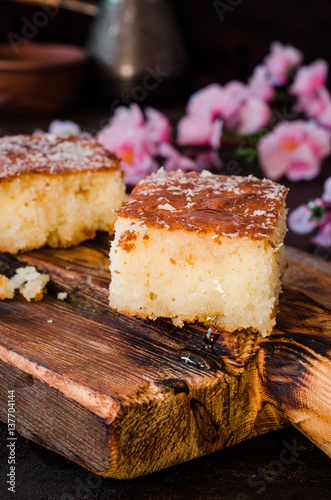 Sweet pie Basbousa or revane or Namoora on wooden plate and dark background with spring flowers. Arabian cuisine. Selective focus