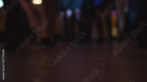 Crowd of people dancing on a dancefloor, close-up footage of people actively moving their feet to the music. Dancing legs with disco lights.