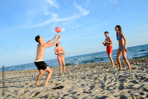four young people man and woman playing beach volley together by the sea in sunny summer vacation day