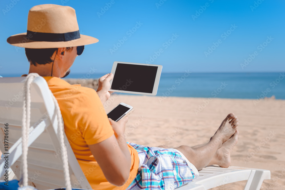 Closeup of business man holding in hands using tablet pc computer on sunny beach outdoors. Top view mock up travel vacation background
