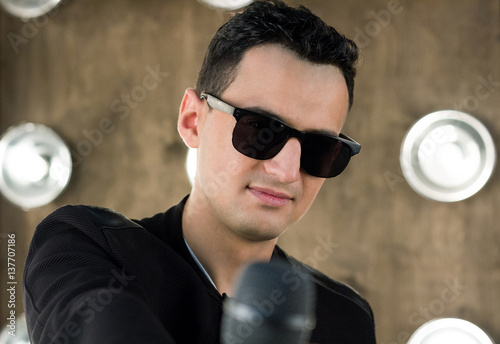 Male singer in sunglasses with microphone performs in projectors lights photo