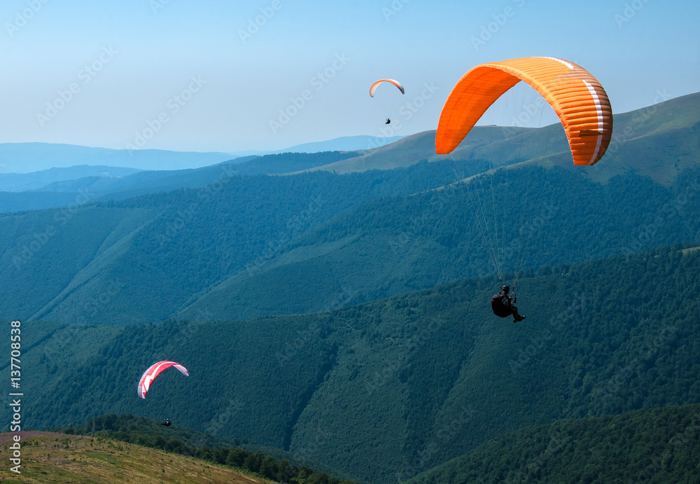 Paragliding in the sky. Two paraglider fly over the tops of the mountains in summer sunny day. Carpathians, Ukraine. Paragliding in the sky. Two paraglider fly over the tops of the mountains in summer sunny day. Carpathians, Ukraine.