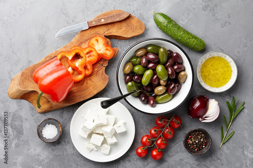 Greek salad basic ingredients: fresh olives, feta cheese, tomatoes, pepper, cucumbers and olive oil on stone background