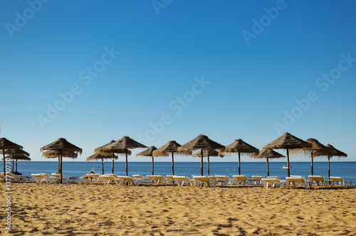 Straw umbrellas on ocean beach in Algarve Portugal, sunny outdoors background © aquar
