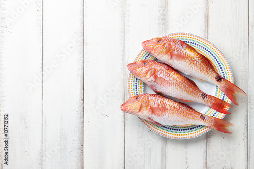 Fresh red mullet fish on plate on white wooden background