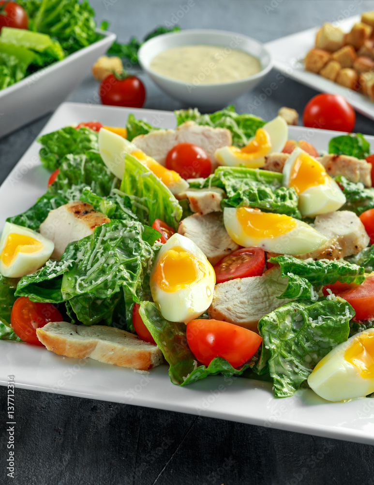 Fresh healthy Caesar salad with chicken, eggs, tomatoes, Cheese and Croutons on white plate Fresh healthy Caesar salad with chicken, eggs, tomatoes, Cheese and Croutons on white plate