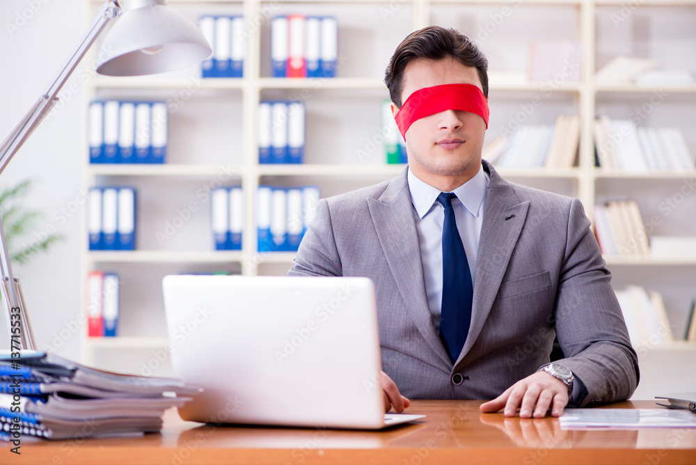 Blindfold businessman sitting at desk in office Blindfold businessman sitting at desk in office