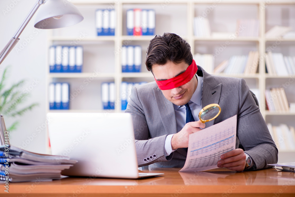 Blindfold businessman sitting at desk in office Blindfold businessman sitting at desk in office