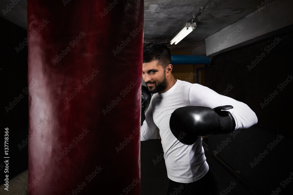 Handsome young boxer is exercising with boxing gloves and punching bag at the gym