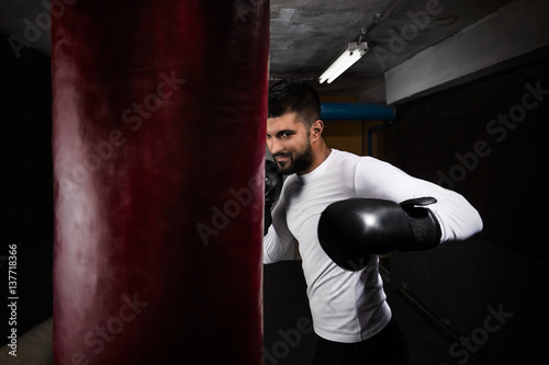 Handsome young boxer is exercising with boxing gloves and punching bag at the gym © bokan
