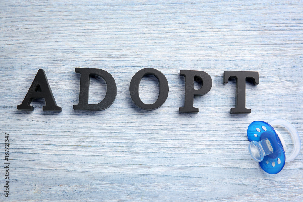 Word ADOPT and passifier on light wooden background Word ADOPT and passifier on light wooden background