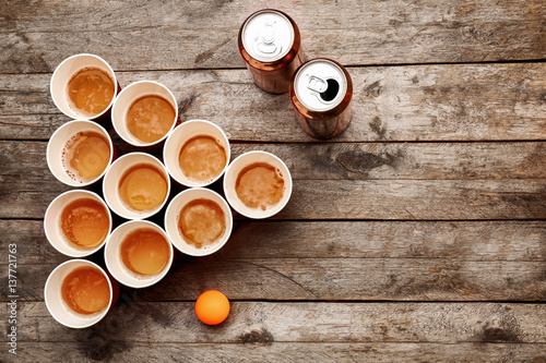 Plastic beer pong cups and cans on wooden table, top view