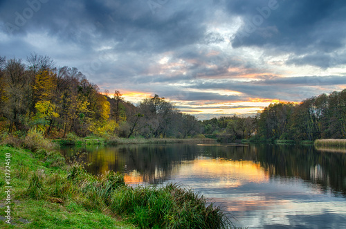 Sunset on the lake with forest with green grass in summer.