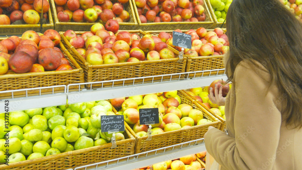 Woman selecting fresh red apples in grocery store produce department and putting it in plastic bag. Young pretty girl is choosing apples in supermarket and putting them into shop basket. Close up