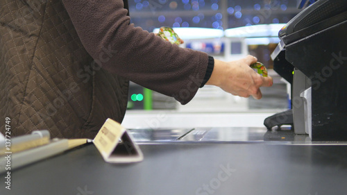 Shopper paying for products at checkout. Foods on conveyor belt at the supermarket. Cash desk with cashier and terminal in hypermarket. Working of cashier. Shopping at store. Close up