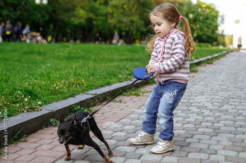 Girl in a pink striped blouse and blue jeans pulling dog