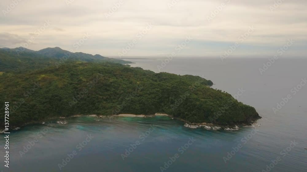 Wild beautiful beach with coconut palms. Aerial view: sea and the tropical island with rocks, beach and waves. The coast of the tropical island with the mountains and the rainforest on a background of Wild beautiful beach with coconut palms. Aerial view: sea and the tropical island with rocks, beach and waves. The coast of the tropical island with the mountains and the rainforest on a background of