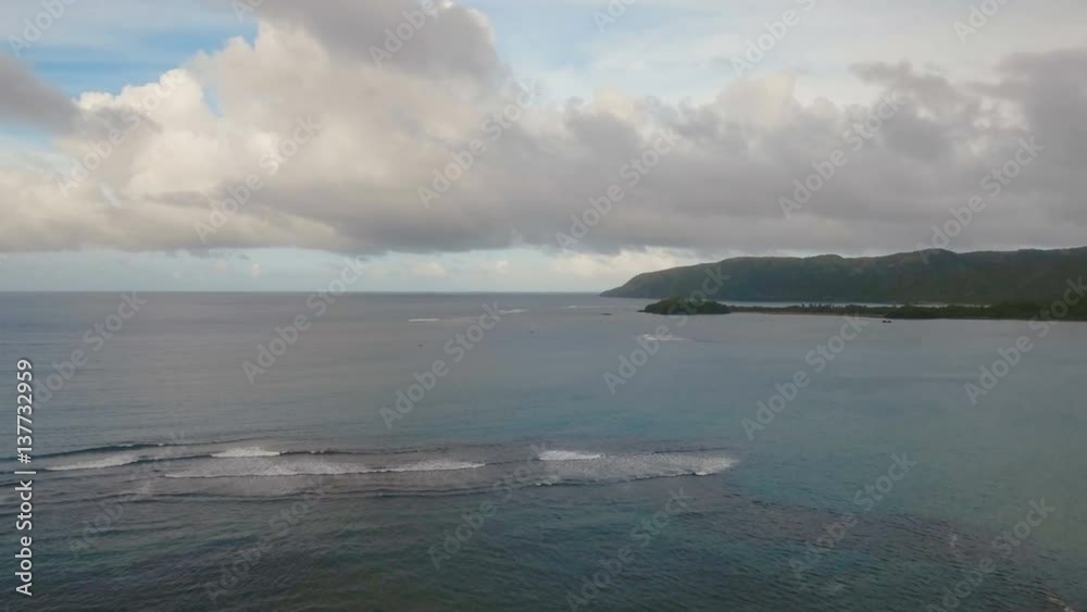 The coast of the tropical island with the mountains and the rainforest on a background of ocean with big waves.Aerial view: sea and the tropical island with rocks, beach and waves. Seascape: sky The coast of the tropical island with the mountains and the rainforest on a background of ocean with big waves.Aerial view: sea and the tropical island with rocks, beach and waves. Seascape: sky
