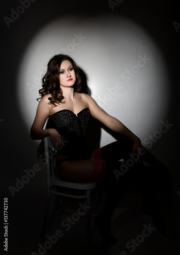 Sexy girl in lacy lingerie and corset, sitting on chair posing in the studio a dark background