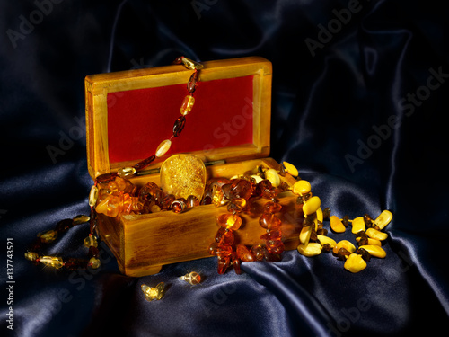 Wooden chest with a bunch of jewelry from authentic Baltic amber with a big pendant in the center, on a blue background satin.