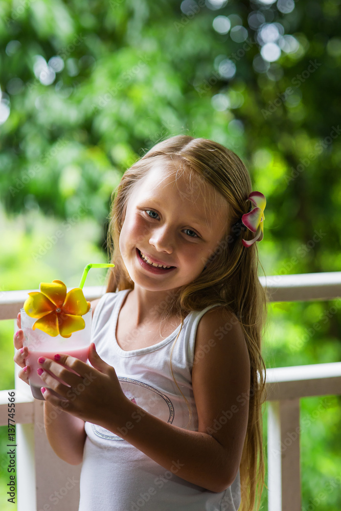 happy little girl with long hair on the balcony of a resort in the morning with a glass of milk happy little girl with long hair on the balcony of a resort in the morning with a glass of milk