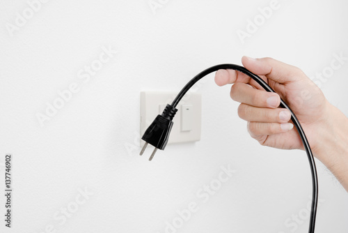 Hand of man unplug electric outlet plug on wall white background safety concept photo
