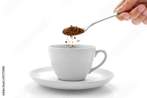 Hand pours instant coffee from a spoon in a coffee cup