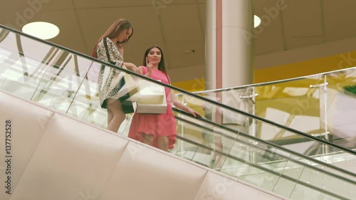 Two pretty women standing on the down escalator of a shopping mall