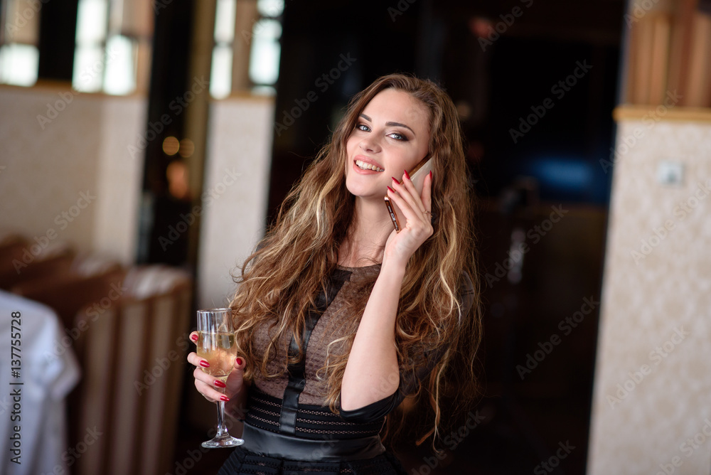 Beautiful girl drinking champagne and talking on the phone in the restaurant