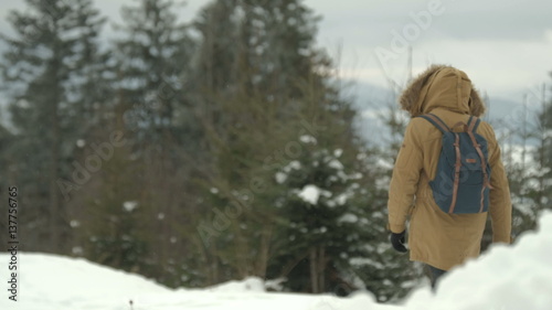 man goes through the snowy winter forest in a brown jacket with a hood and a backpack © puzurin