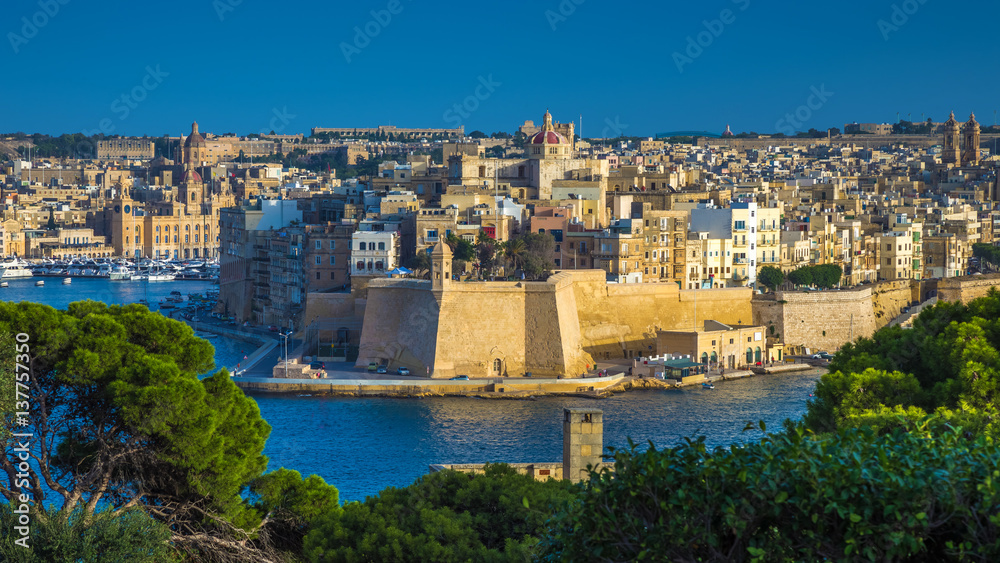 Valletta, Malta - The view from Valletta with trees, Island of Senglea, Gardjola Gardens with watchtower, the Grand Harbour with boats and ships and clear blue sky