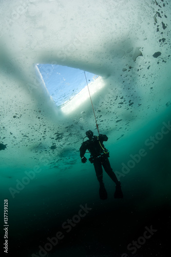 Scuba diver looking at ice hole, while ice diving