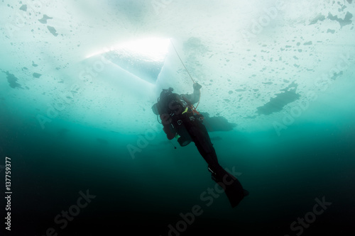 Scuba diver looking at ice hole, while ice diving
