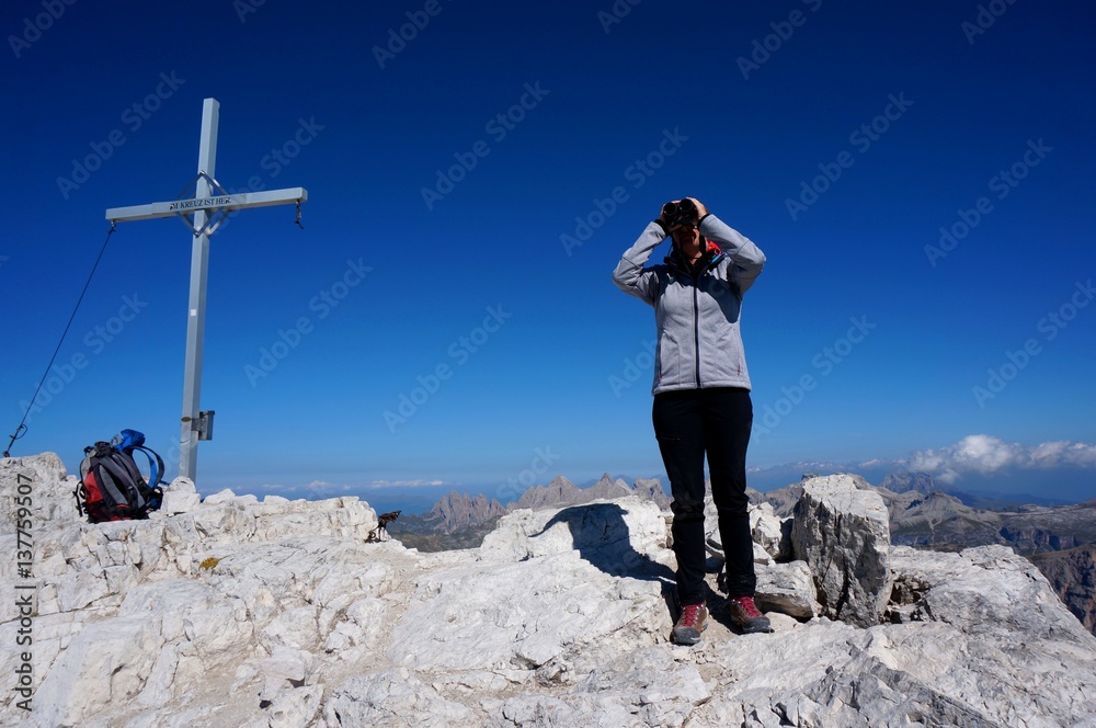 Obraz premium Wanderin erkundet Umgebung mit Fernglas neben Gipfelkreuz 