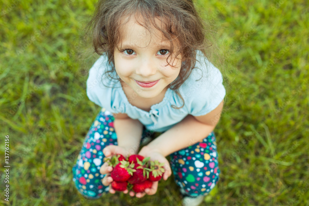 Portrait of small smiling girl with a handful of just gathered big strawberries in a garden Portrait of small smiling girl with a handful of just gathered big strawberries in a garden