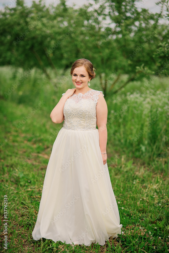Young overweight girl at beige dress posed background spring garden. Young overweight girl at beige dress posed background spring garden.